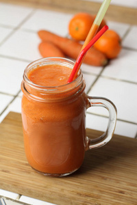 橙色健康清爽蔬菜胡萝卜冰沙在透明的玻璃与小管在白色的桌子，健康营养饮食排毒
