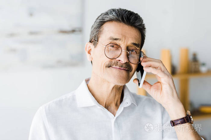 戴眼镜的开朗的老人在家里谈论智能手机
