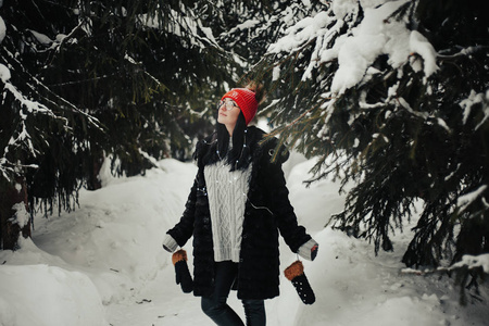 令人惊奇的女孩的肖像，摆着长长的黑发，在寒冷的冬天挥手。 户外照片梦幻女子穿着羊毛红色帽子，戴着圆形眼镜，站在雪地公园。 近毛皮