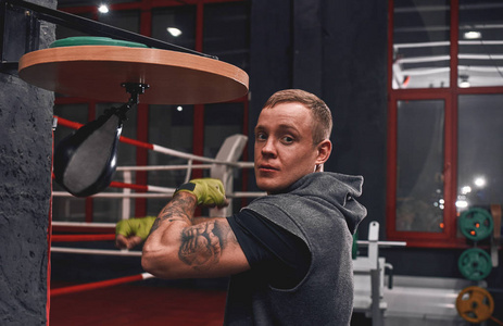 他是个新冠军。在拳击健身房里, 一个手臂锻炼专业的年轻拳击手用绿色的手包裹着打打气筒速度包