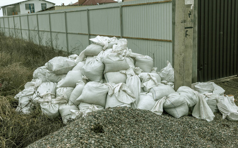 白色建筑垃圾麻袋被倾倒在正在施工的围栏附近的堆中。 污染概念。 垃圾填埋场垃圾场中的垃圾。 非法垃圾场回收