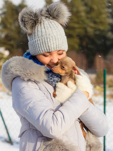 年轻女子在外面雪地里玩得很开心。雌性在寒冷的冬天和她的小纯种狗小狗玩耍。