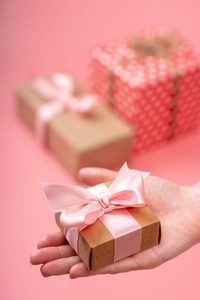 s hands holding gift box Packed in Kraft paper on pink backgroun
