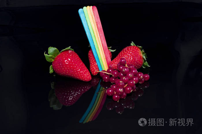 黑色背景反光表面有彩虹旗颜色的草莓和醋栗