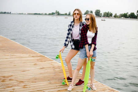 两个穿着嬉皮士服装的快乐溜冰女孩在暑假期间在木制码头上玩耍