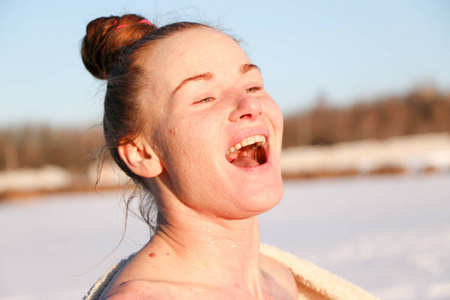 一个美丽的年轻女孩，一个红头发的女人，在一个美丽的晴天在湖上游泳后，微笑着享受阳光。 在雪景和蓝天的背景下。 乌克兰苏米州什斯特