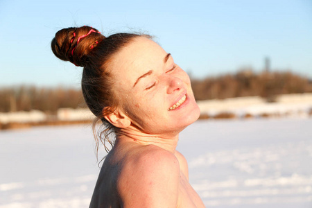 一个美丽的年轻女孩，一个红头发的女人，在一个美丽的晴天在湖上游泳后，微笑着享受阳光。 在雪景和蓝天的背景下。 乌克兰苏米州什斯特
