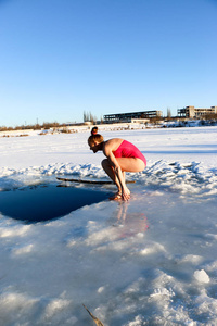 一个美丽的年轻女孩，一头红色的头发，一件粉红色的泳衣，准备在一个美丽的阳光明媚的日子里潜入湖面上的冰水中。 乌克兰苏米州什斯特卡