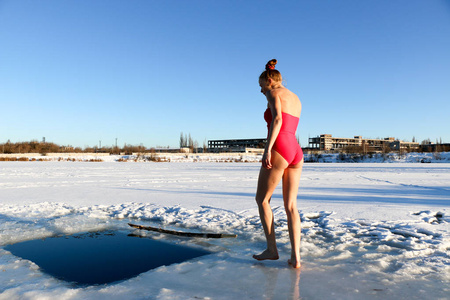 一个美丽的年轻女孩，一头红色的头发，一件粉红色的泳衣，准备在一个美丽的阳光明媚的日子里潜入湖面上的冰水中。 乌克兰苏米州什斯特卡