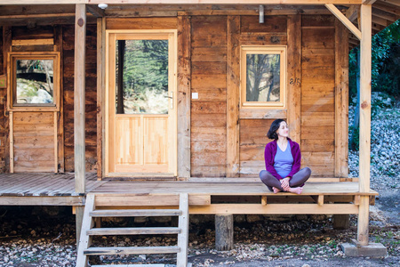 一个女人坐在一座旧木屋的门廊上。 在温暖的春天，赤脚女孩在房子附近休息。