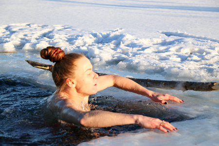 一个美丽的年轻女孩，红头发，一件泳衣潜入冰冷的水在冬天的湖面上，在一个美丽的阳光明媚的日子。 乌克兰苏米州什斯特卡