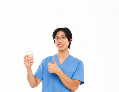 微笑的亚洲男子医生穿着制服，站在白色背景上，露出杯子，用水竖起大拇指