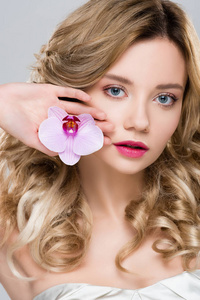 年轻的金发美女，手捧紫色的兰花，与灰色隔离