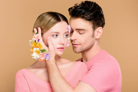 英俊的男人抚摸着女朋友的脸，脸上挂着花，被隔离在米色上