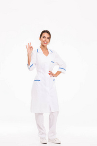 一个自信的年轻女医生穿着制服，站在白色背景上，OK手势。
