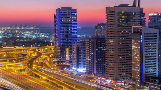 迪拜码头与交通谢赫扎耶德道路全景白天到晚上过渡时间灯打开。 阿联酋摩天大楼的夜间照明。 来自JLT的鸟瞰图