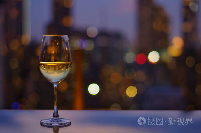 一杯白酒在屋顶酒吧的桌子上,五颜六色的城市灯光和文字空间.