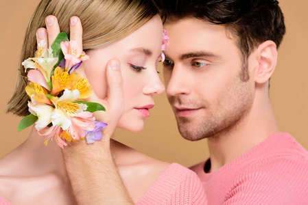 英俊的男人抚摸着漂亮的女朋友的脸，脸上挂着花，被隔离在米色上