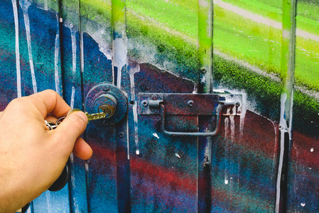 s hand using a key to open the lock of a door of an abandoned ga