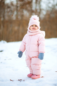 穿着粉红色连衣裙的小女孩在下雪的冬季公园里微笑