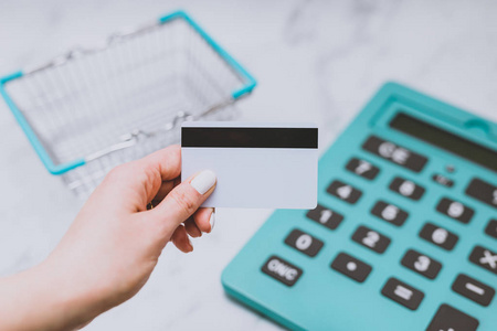 s hand holding payment card in front of huge calculator and shop