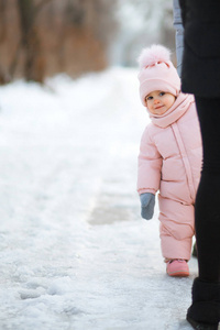 美丽的年轻女孩穿着一件粉红色的连体衣，在一个下雪的冬天公园里从人们身后偷看。 小孩在雪地森林里玩耍和跳跃