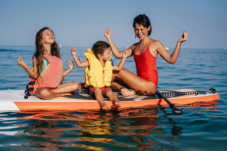 妈妈和两个小女儿在划桨板上做瑜伽