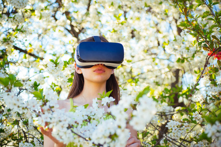游戏和娱乐。虚拟技术模拟。年轻的女士在春天绽放时戴着 vr 眼镜。可爱的女孩在春天的花园玩。漂亮的女孩在虚拟现实耳机。创新的 v