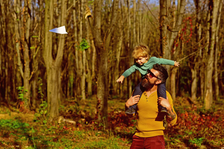 小男孩梦想在父亲的肩上飞得很高。 父子在公园发射纸飞机。 不管发生什么，驾驶飞机。