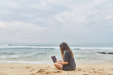 在海滩上的电脑前工作的年轻女孩。在海滩上工作的自由职业者