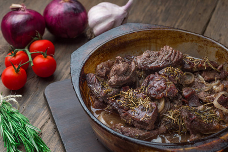 肉与迷迭香炖在玻璃碗在乡村木制背景与新鲜蔬菜。
