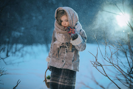 小女孩带着篮子去寻找冬天在森林里的雪下的第一朵花