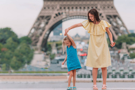 可爱的小女孩和她年轻的妈妈在巴黎附近的埃菲尔铁塔在暑假期间