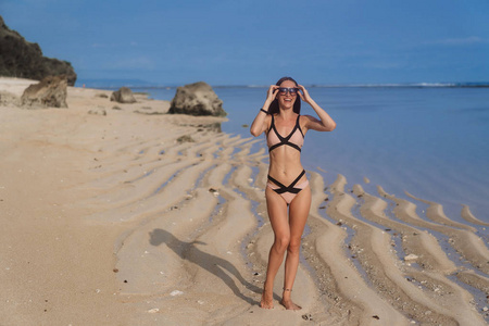 的女孩在泳衣与太阳镜摆姿势在沙滩上