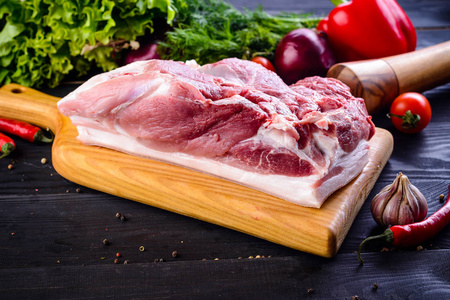 生猪肉。 新鲜牛排在木切割板上的深色背景。 生猪肉肩配蔬菜及香料