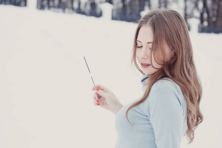 快乐和微笑的女孩在下雪时保持街道上的孟加拉灯。 冬季概念。 新年概念。