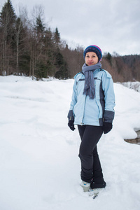 穿裤子的女孩戴着手套和围巾站在森林前的雪地里