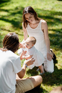 穿着白色衣服微笑的家长正在教小女儿如何在草坪上迈出第一步