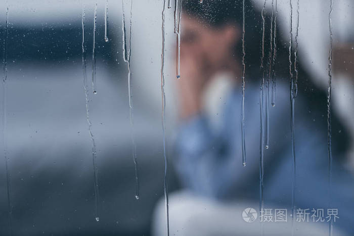 雨滴选择性地聚焦在窗户上,悲伤的女人坐在背景上