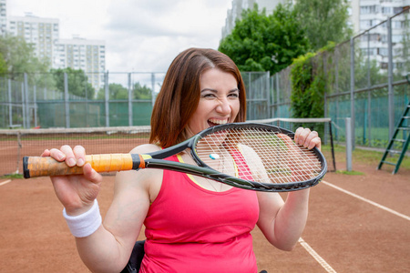 成功的女运动员在网球场上咬球拍。健康的生活方式