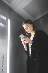 忙碌的年轻女员工正在电梯里看她的智能手机屏幕。 垂直射击的女商人在电梯使用她的智能手机。