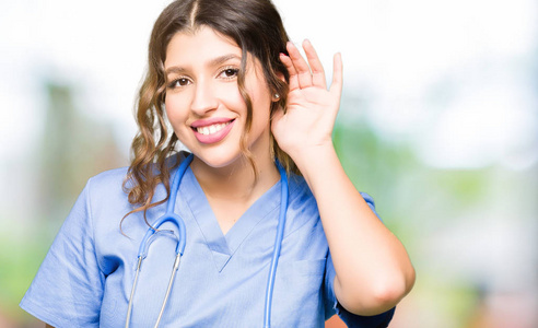 年轻的成年医生女士穿着医疗制服，微笑着用手捂住耳朵听谣言或流言蜚语。 耳聋概念。