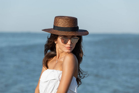 在阳光明媚的日子里, 在海边, 穿着白色太阳镜和帽子的黑头发女孩的肖像