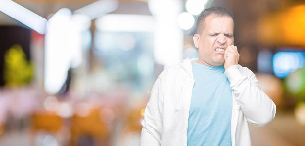 中年阿拉伯男子穿着运动衫，在孤立的背景上看起来压力和紧张，双手咬着嘴的指甲。焦虑问题。