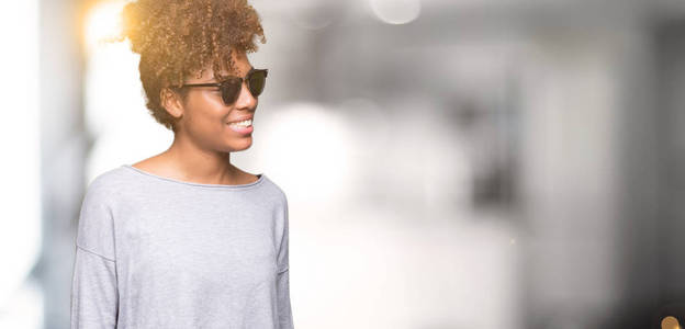 美丽的年轻的非洲裔美国妇女戴着太阳镜，在孤立的背景上看着一边，脸上带着微笑，自然的表情。充满自信的笑。