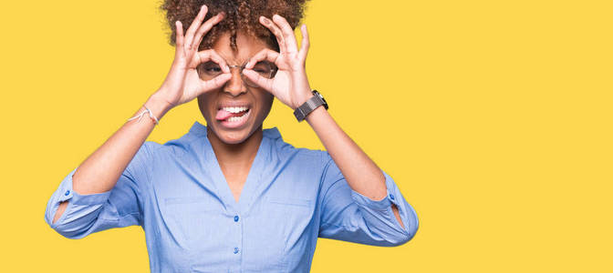 美丽的年轻非裔美国商务女性，在孤立的背景下做着好的手势，比如双筒望远镜伸出舌头，眼睛透过手指看。疯狂的表情。