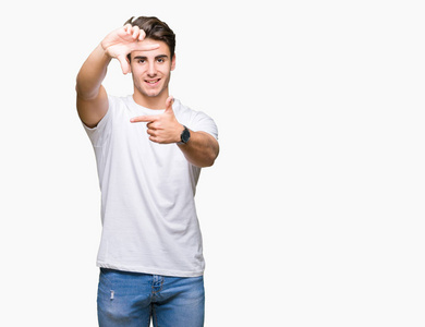 年轻的帅哥穿着白色的t恤，在孤立的背景上微笑，用手和手指制作框架，用快乐的脸。创意和摄影理念..