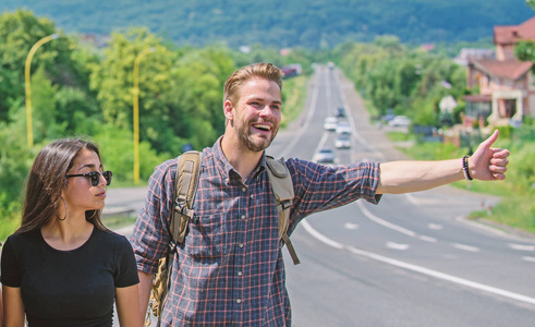 情侣旅行的人和女孩搭便车在边缘道路自然背景。搭便旅行。情侣搭便车旅行夏日阳光明媚的一天。搭便车是最便宜的旅行方式之一