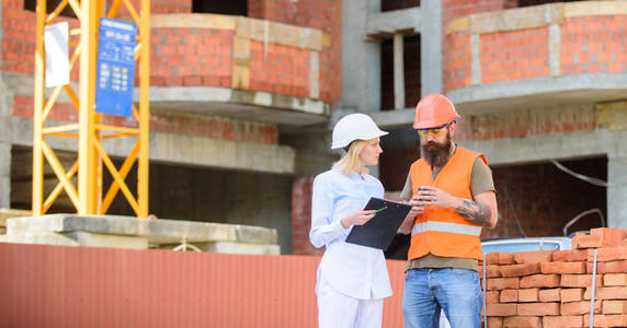 施工团队沟通理念。建筑客户与建筑行业参与者之间的关系。女工程师和建筑工人在建筑工地进行沟通。讨论计划