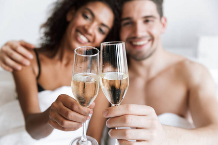 一对美丽快乐的年轻多民族夫妇在毯子下放松，从眼镜里喝着闪闪发光的香槟